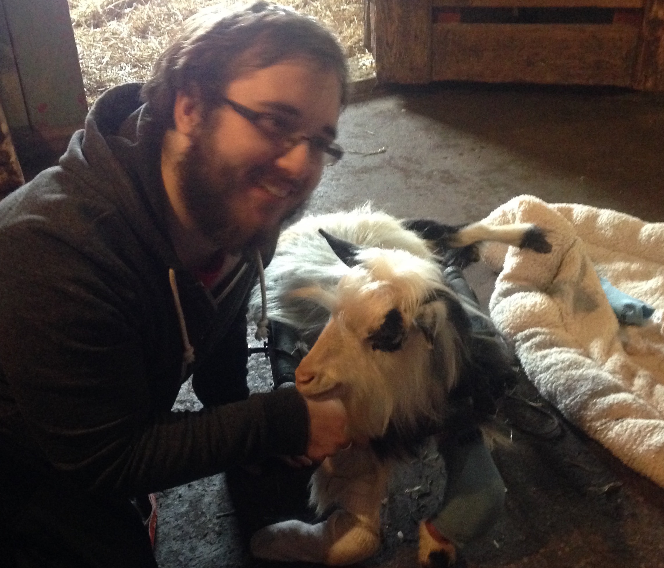 An image of me posing with a paraplegic goat and the mobility cart I made for him